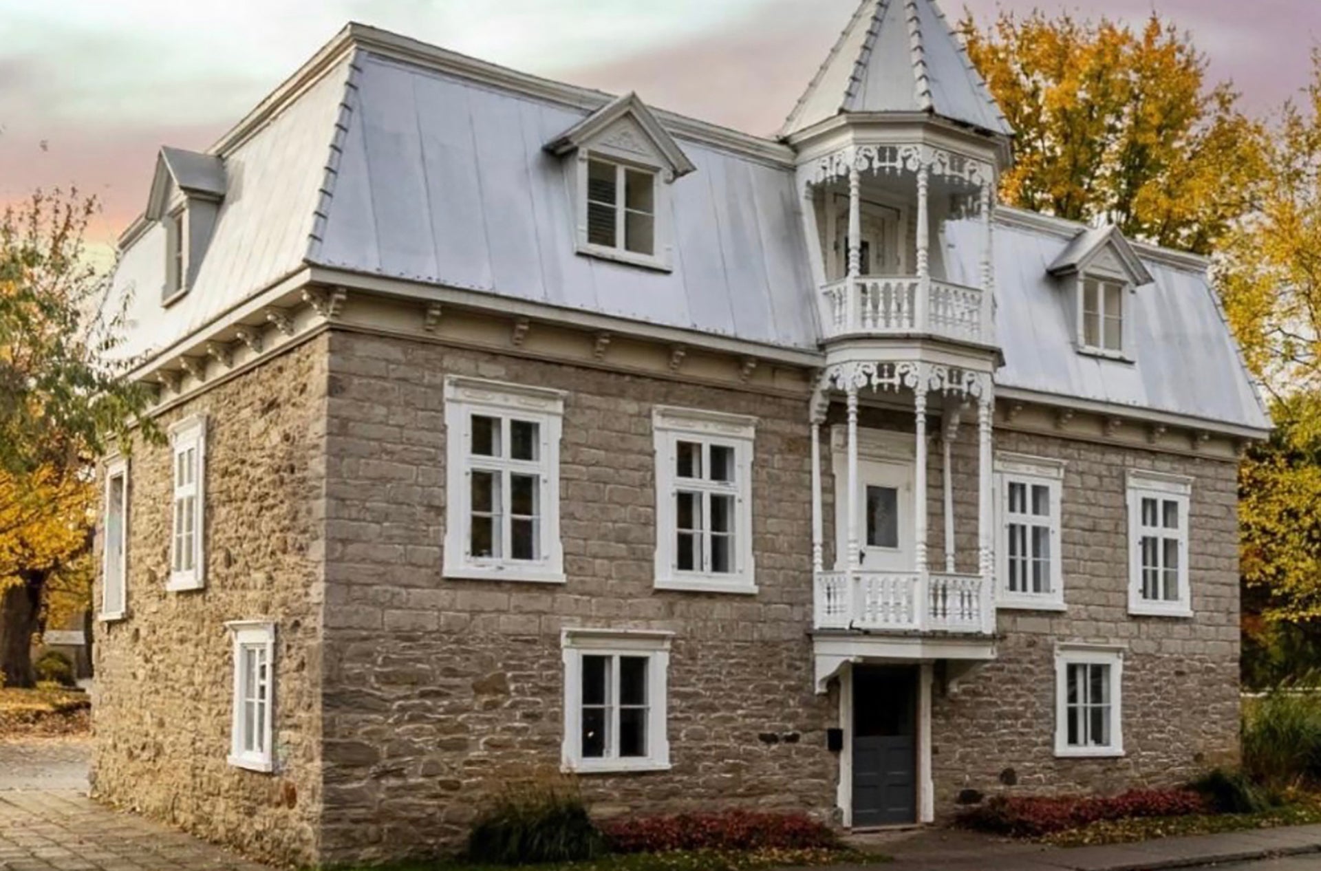 Maison Jacynthe Laval |Façade en pierre de la maison patrimoniale Papineau-Cléroux à Laval, avec toit mansardé et balcons blancs ouvragés.