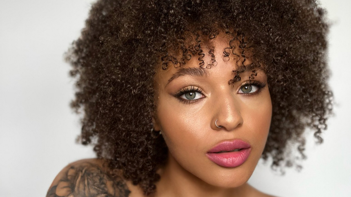 Femme à la peau foncée portant un maquillage lumineux aux lèvres roses et aux yeux soulignés.